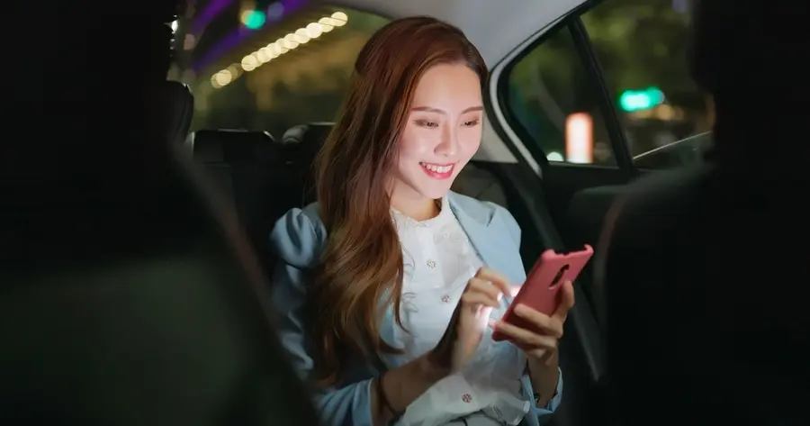 A girl is smiling using her smartphone utilizing a Black Car Service during the nighttime. symbolizing Houston Black Car & Chauffeur Services.